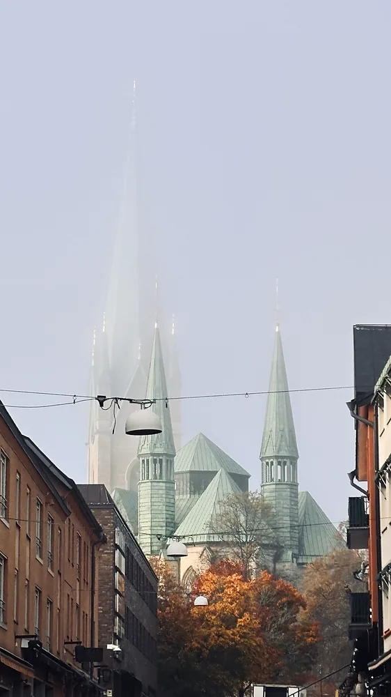 Kyrkspiror i morgondimma ovanför en stadsgata