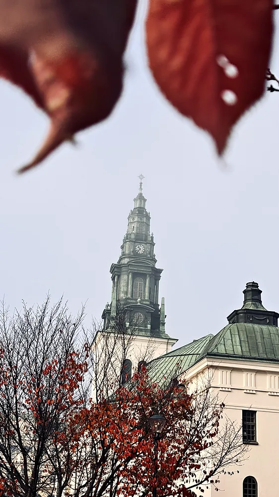 Kyrktorn med kopparkupol inramat av röda höstlöv