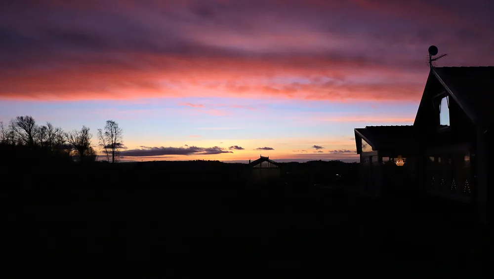 Silhuett av en gård mot en rosa och lila kvällshimmel