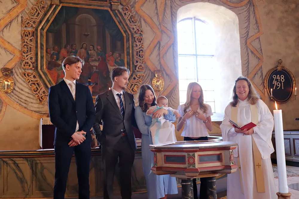 Familj samlad vid dopfunten i en målad kyrka