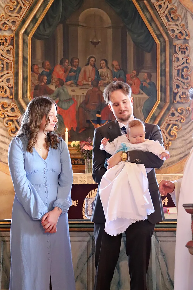 Föräldrar med sitt döpta barn framför kyrkans altartavla